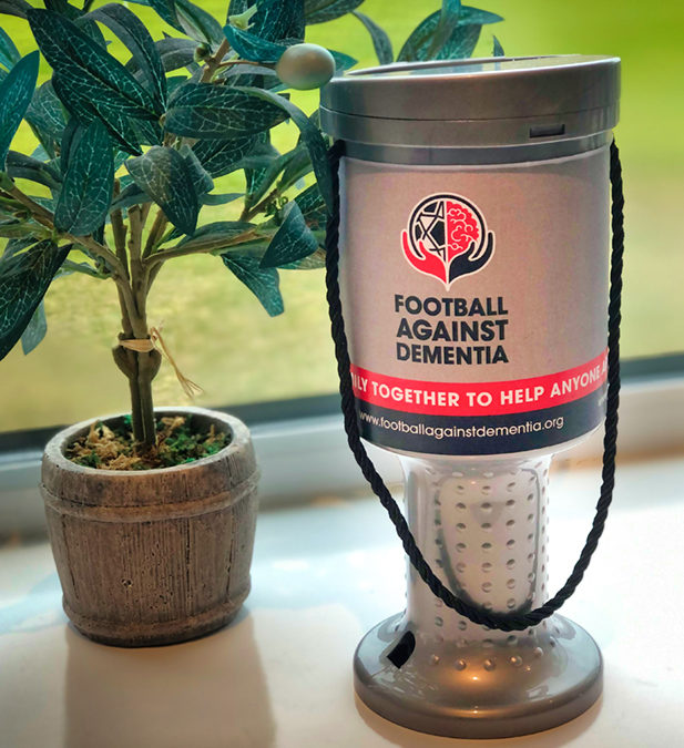 Photograph of a charity collection box on a window sill next to a small olive tree